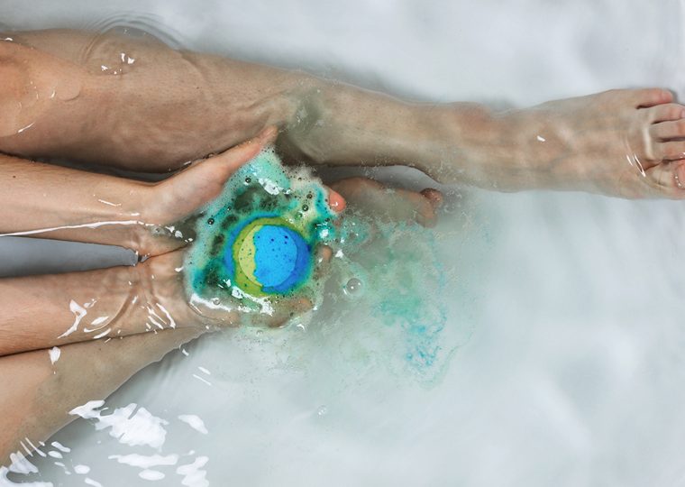 Person holding bath bomb while sitting in tub