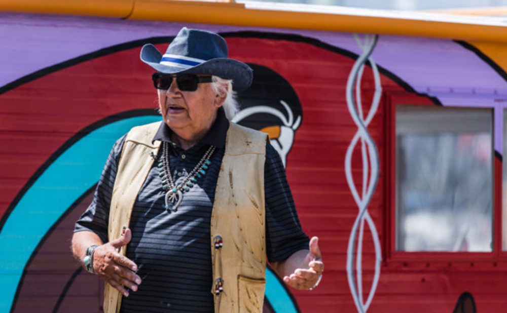 Elder Duke Redbird speaking in front of painted house boat