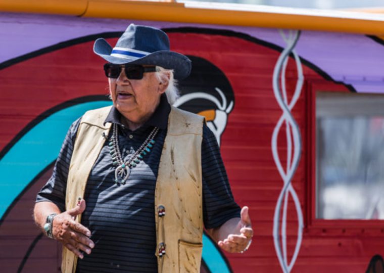 Elder Duke Redbird speaking in front of painted house boat