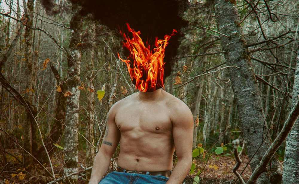 Shirtless man in woods with head on fire