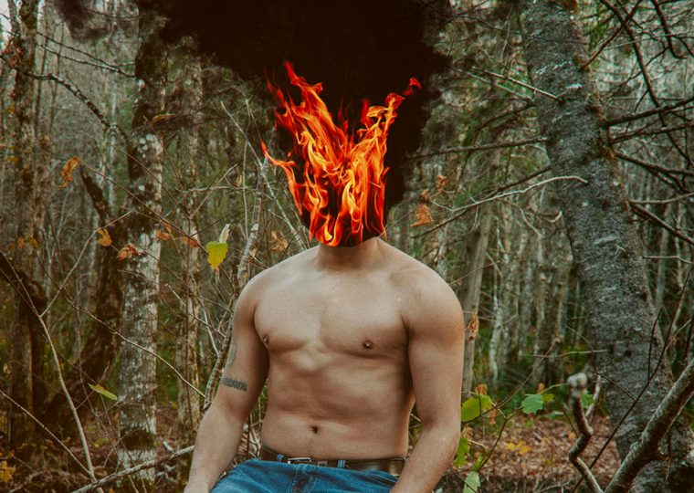Shirtless man in woods with head on fire
