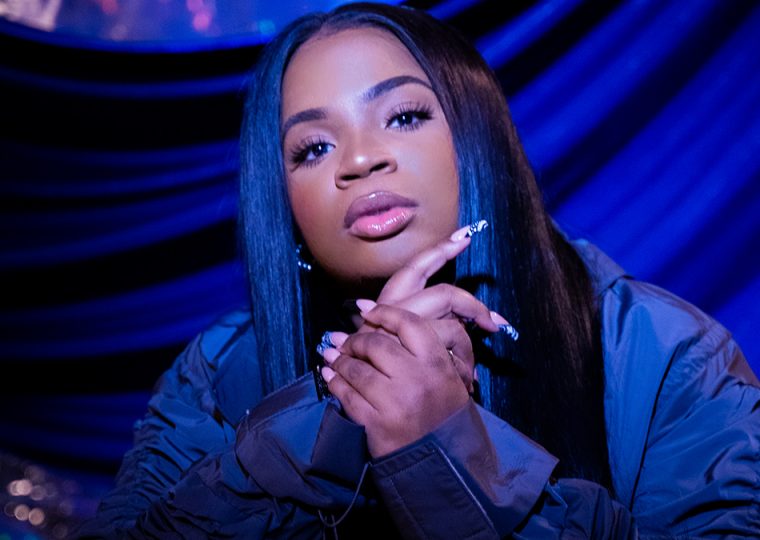 Savannah Re posing in front of draped blue fabric.