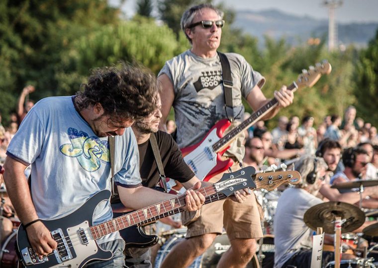 A guitarist and bassist performing outside on stage at a concert.