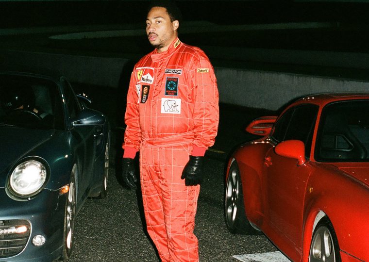 Cadence Weapon standing between two sports cars.