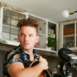 Sam Drysdale sitting, holding his guitar