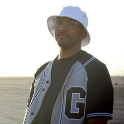 Space Ghost standing outside in the sun wearing a white bucket hat.