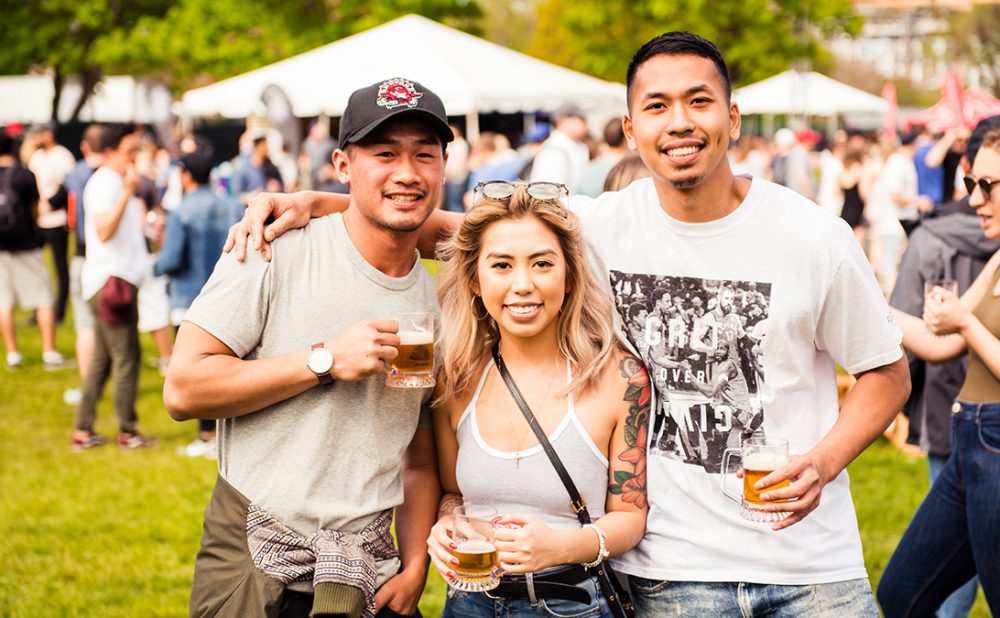 Two men and a woman posing outdoors at a beer festival.