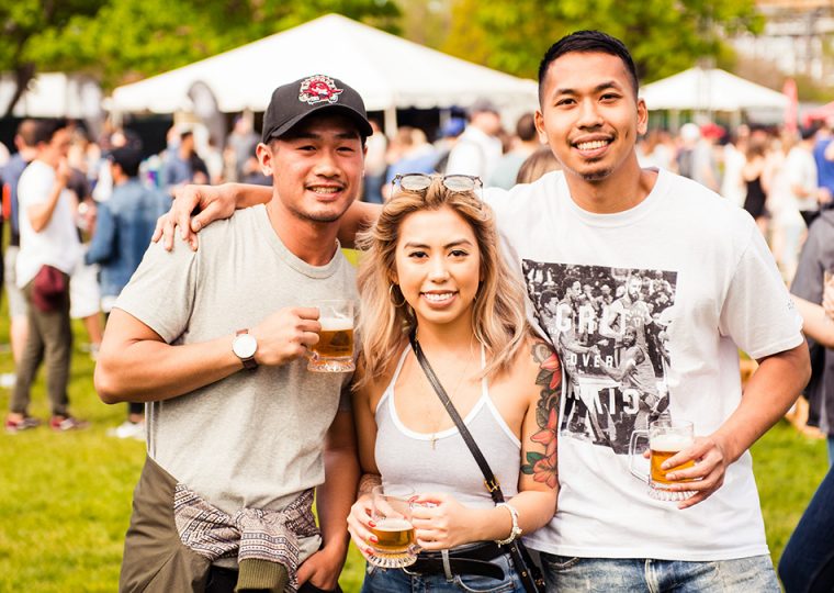 Two men and a woman posing outdoors at a beer festival.