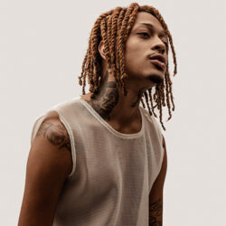 Nue standing angled in a beige sleeveless tee against a beige background.