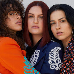 Three members of MUNA standing cheek to cheek.