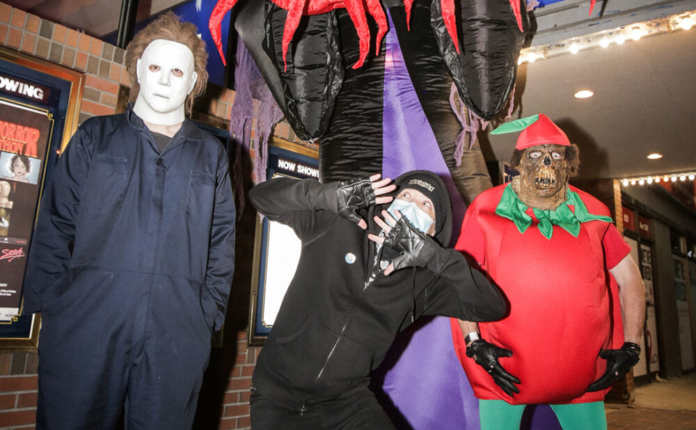 Three people dressed in Halloween costumes outside a movie theatre