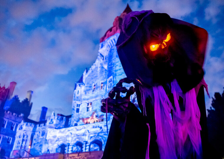 Cloaked ghoulish figure with glowing orange eyes in the foreground with Casa Loma in the background.