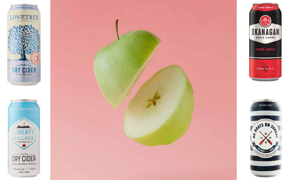 Four different cans of hard cider, flanking an apple that's been sliced in half mid-air.
