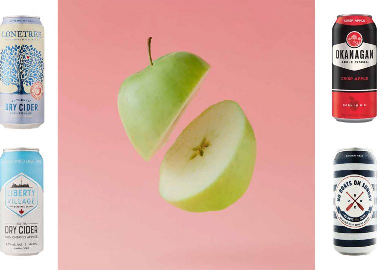 Four different cans of hard cider, flanking an apple that's been sliced in half mid-air.