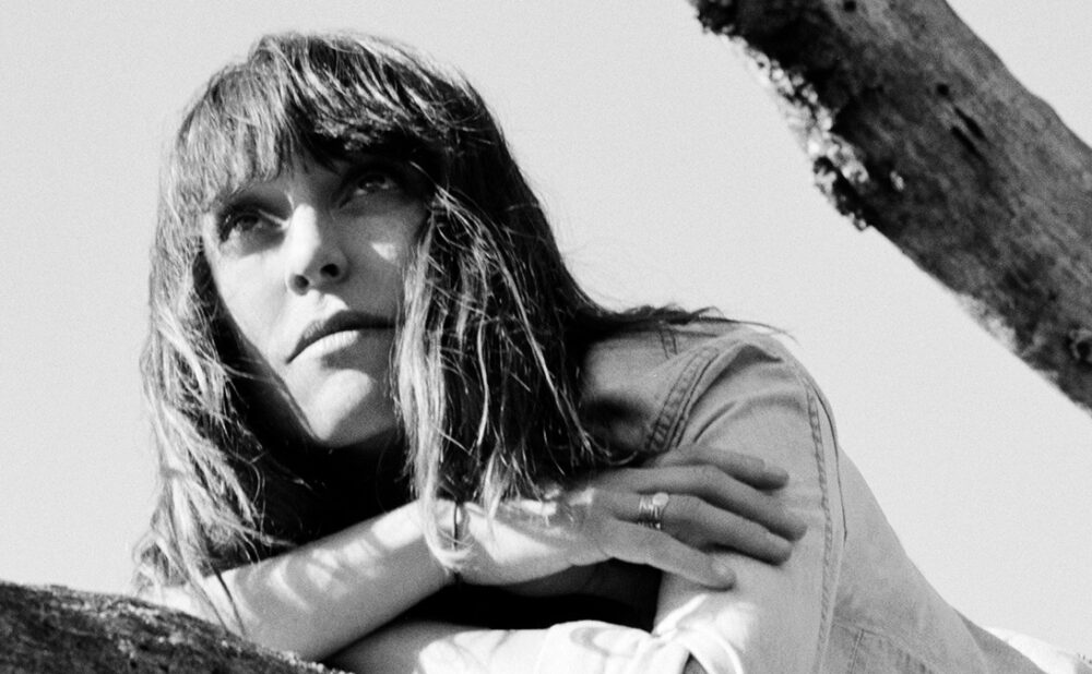 Black and white photo of Feist leaning on a branch, looking into the distance.