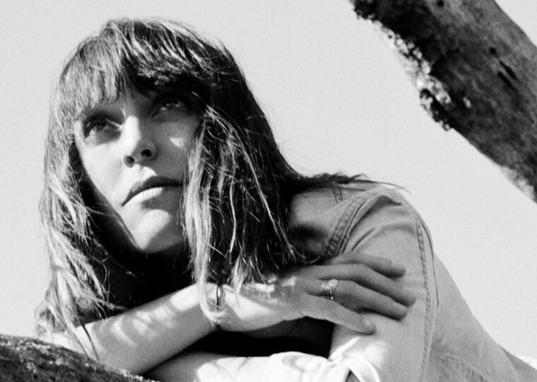 Black and white photo of Feist leaning on a branch, looking into the distance.