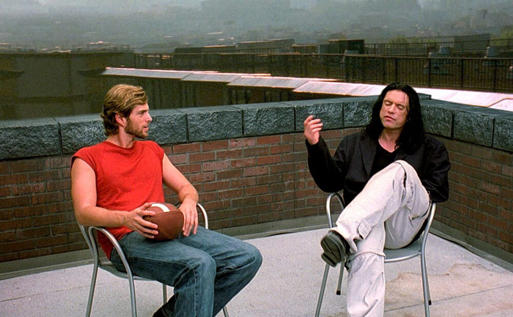 A scene from The Room with two characters sitting in chairs on a rooftop.