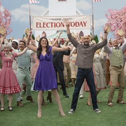 A crowd of people with their hands in the air in front of a sign that reads 