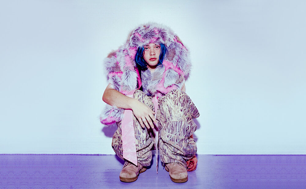 347aidan posing in a squat against a light background, on a lavender coloured floor.