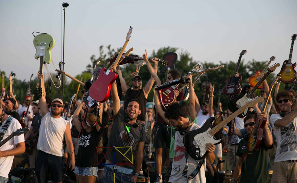 Crowd of people holding their hands up, some of them are holding up guitars.
