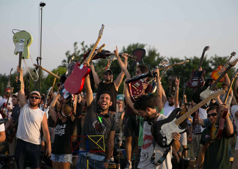 Crowd of people holding their hands up, some of them are holding up guitars.