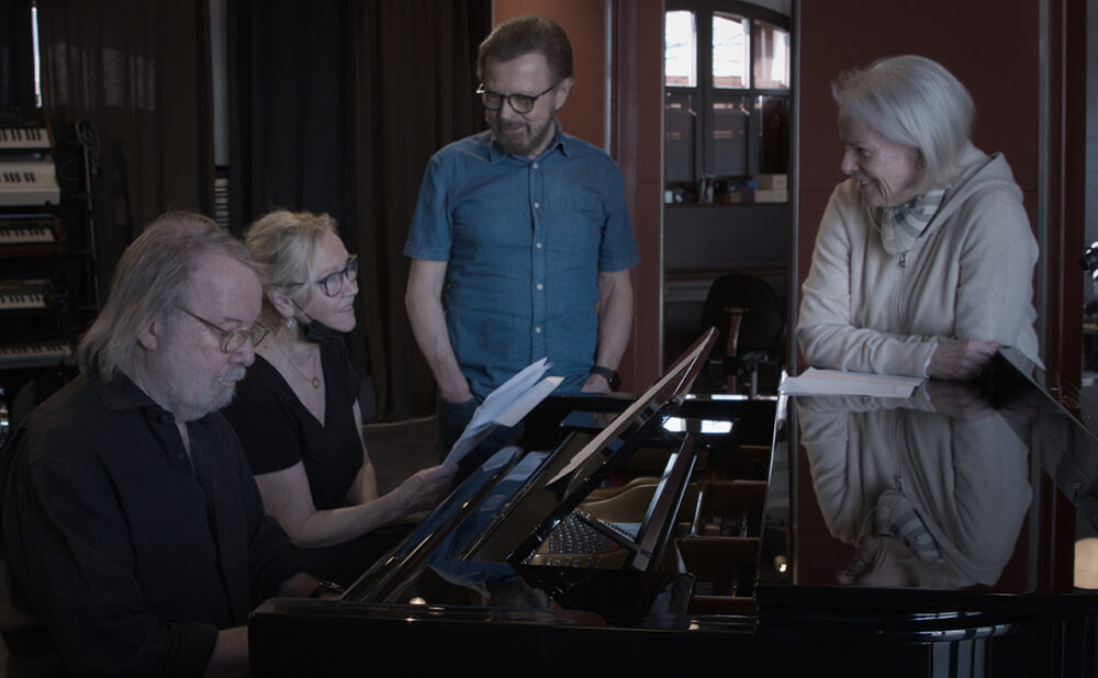 Members of ABBA standing around a piano in a recording studio.