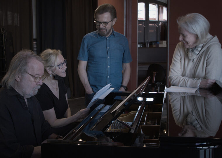 Members of ABBA standing around a piano in a recording studio.