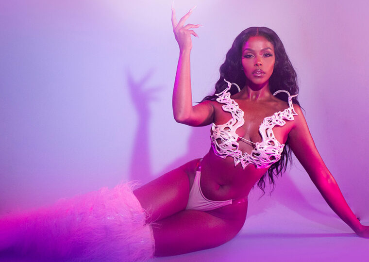 Amaal sitting on the ground with her legs outstretched to her right as she poses with one hand in the air.