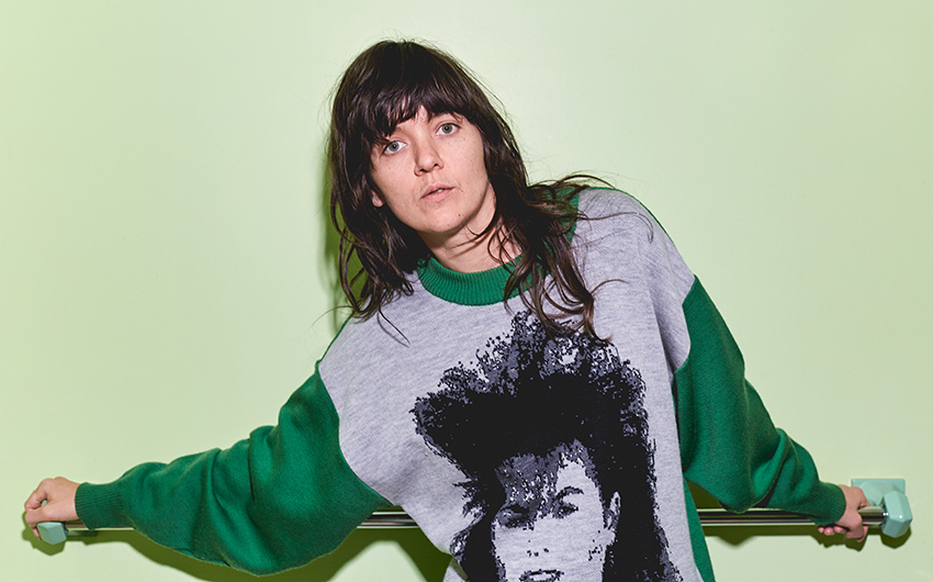 Courtney Barnett in a green and grey sweatshirt against a light green backdrop.