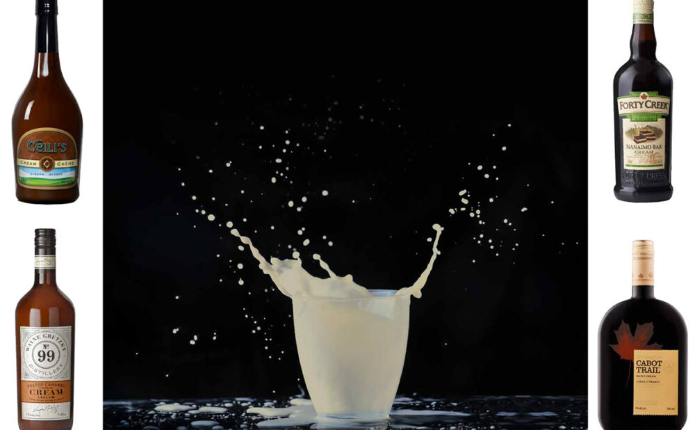 A glass of white milk looking liquid splashing out of the cup, on a black background, with four bottles of cream liquers surrounding it.