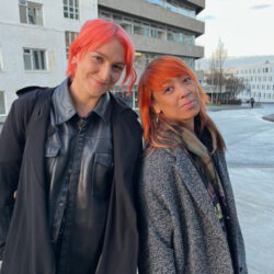 Red Riot standing together, smiling for the camera wearing grey coats outside..