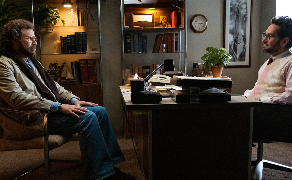 Scene from the show The Shrink Next Door, with Will Ferrell sitting across from Paul Rudd who's seated at a desk.