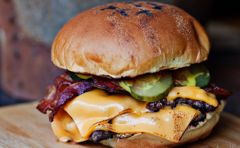 A hamburger with layers of cheese, and bacon and pickles.