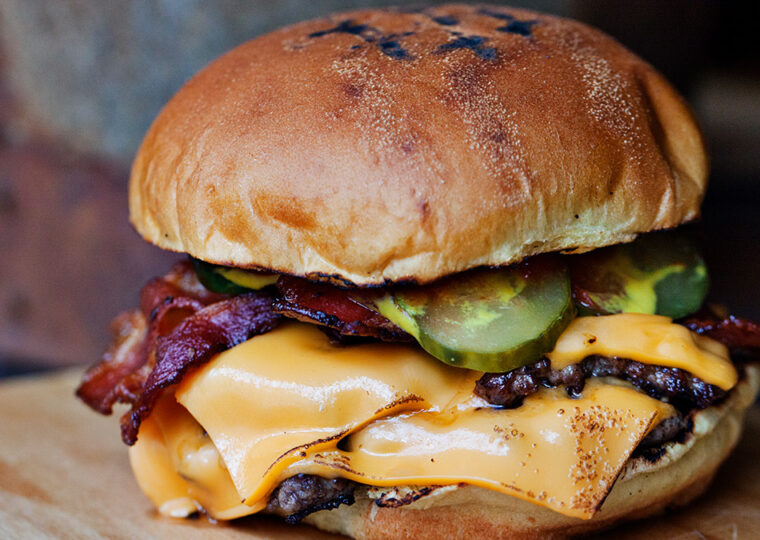 A hamburger with layers of cheese, and bacon and pickles.