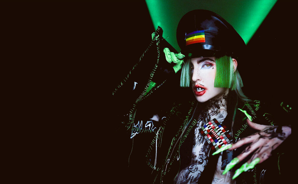 Dorian Electra with green hair in a pleather-looking jacket with long green fingernails.