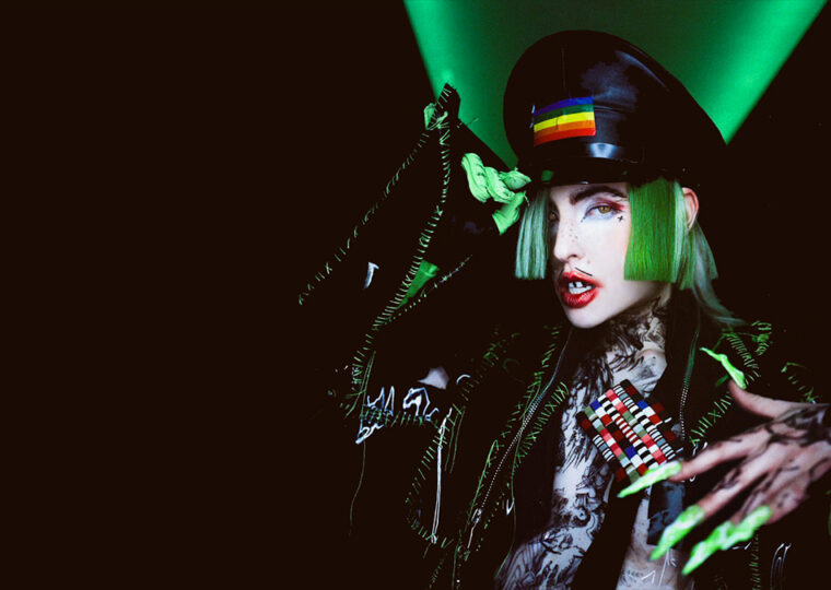 Dorian Electra with green hair in a pleather-looking jacket with long green fingernails.