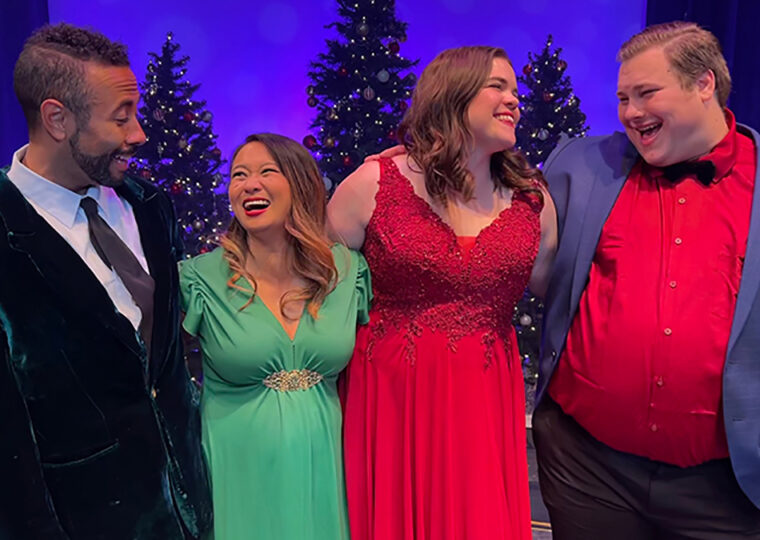 Two men and two women dressed in colourful holiday attire smiling and laughing with each other with on stage in a theatre.