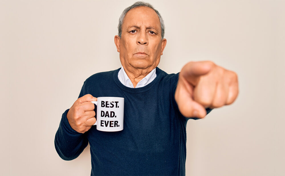Stock photo of a main in a navy blue sweater, pointing at the camera holding a mug that reads