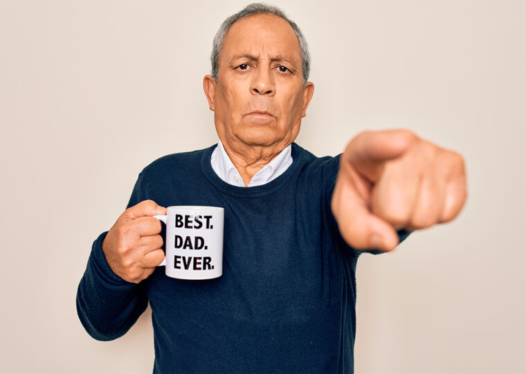 Stock photo of a main in a navy blue sweater, pointing at the camera holding a mug that reads 