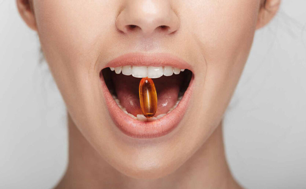 A stock photo of a mouth holding a orange capsule between their teeth.