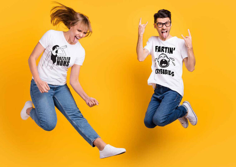 A woman and a man wearing band t-shirts and blue jeans jumping in the air against a yellow backdrop.
