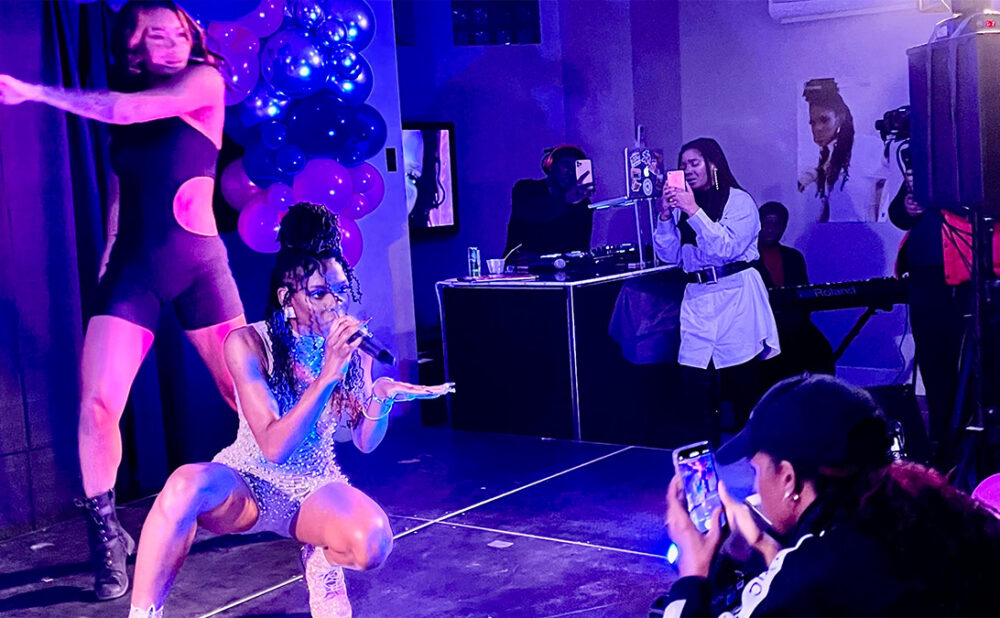 Omega Mighty performing on stage while sister Haviah snaps photo during performance.