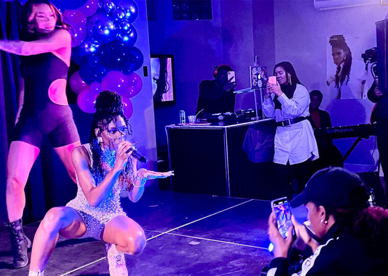 Omega Mighty performing on stage while sister Haviah snaps photo during performance.